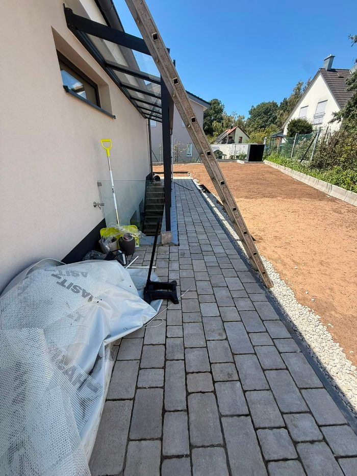Gepflasterter Gehweg entlang der Hausseite mit Kiesstreifen als Spritzschutz