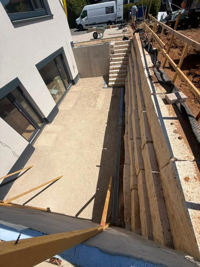 Stützmauer aus Sandsteinblöcken mit Drainagerinne an einem Neubau